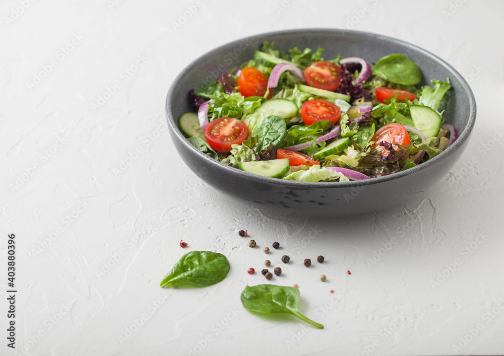 Cucumbers and tomatoes, red onion and spinach mix in fresh vegetables salad in grey bowl plate on white background. Cucumbers and tomatoes, red onion and spinach mix in fresh vegetables salad in grey bowl plate on white background.