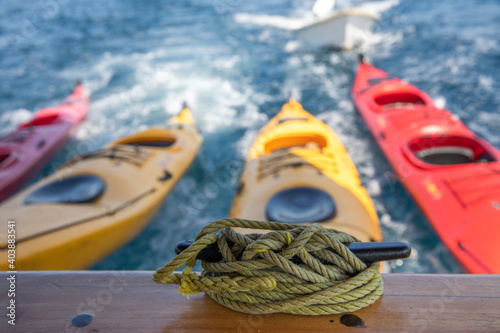 colorful Kayaks bound together towed by a ship and some sailing ropes in the foreground