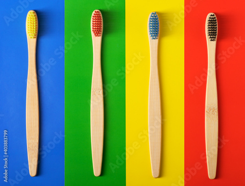 Four colored wooden toothbrushes on a multi-colored background.