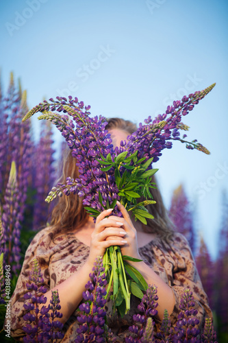 a girl in a summer field with lupins, holding a bouquet of flowers in her hands, in the evening