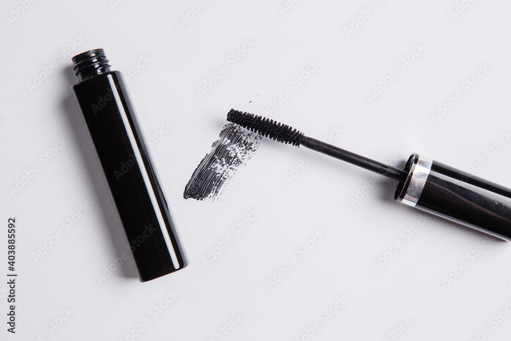 Fototapeta premium smear of black mascara is smeared on a white background, an applicator brush and a tube of black lie next to the smear of mascara
