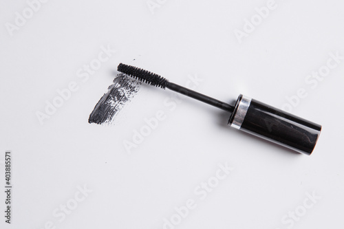 smear of black mascara is smeared on a white background, the applicator brush lies next to the smear of mascara