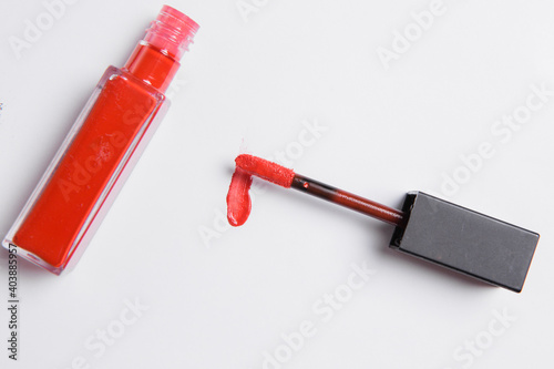 drop of red liquid lipstick smeared on a white background. Red lip gloss in a tube with an applicator on a white background
