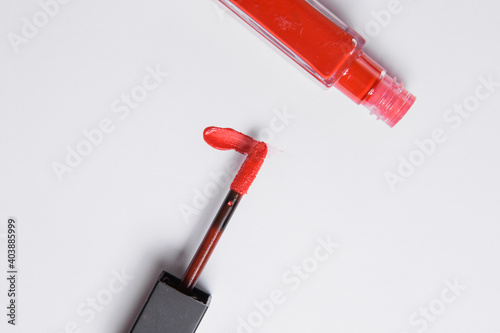 drop of red liquid lipstick smeared on a white background. Red lip gloss in a tube with an applicator on a white background