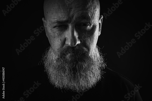 close up photo, portrait of a serious, thoughtful, bearded man on a dark background confident and dramatic looking straight. Concept of male portrait. Black and white photo. Low key