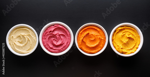 Set of different colorful hummus: classic, beetroot, pepper and pumpkin on a black background top view