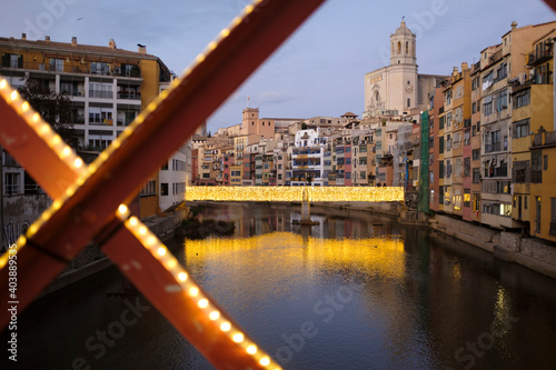 Girona s urban cityscape skyline at dusk with famous gothic cathedral landmark and river houses reflected on a quiet river from red iron bridge