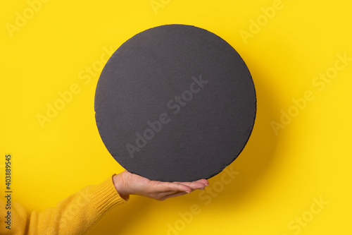 round black slate board on hand over yellow background,  empty space for menu or recipe.