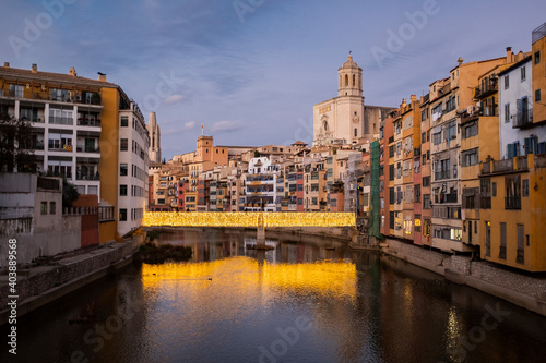 Girona s urban cityscape skyline at dusk with famous gothic cathedral landmark and river houses reflected on a quiet river from red iron bridge