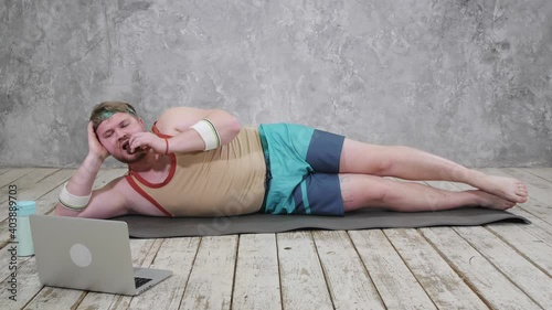 funny fat man doing sports on the yoga mat, doing sports online, looking into the laptop