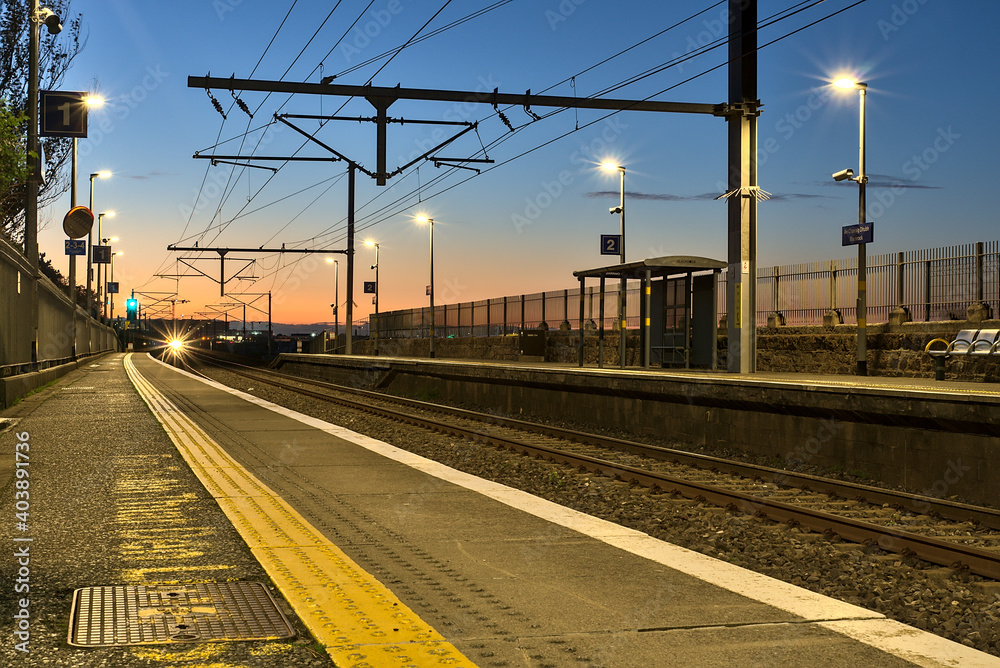 Spectacular view of railway station and colorful sky at Blackrock in the evening, Dublin, Ireland. Lights of the coming train in background