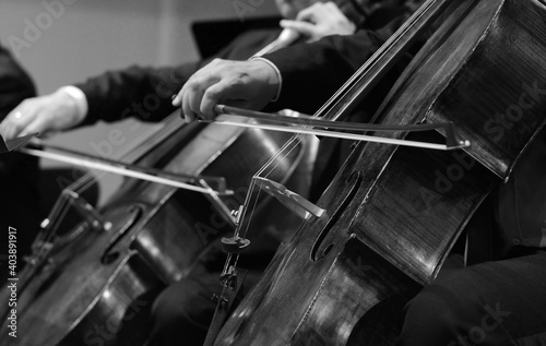 Symphony orchestra on stage, hands playing cello. Professional cello player's hands close up, he is performing with string section of the symphony orchestra