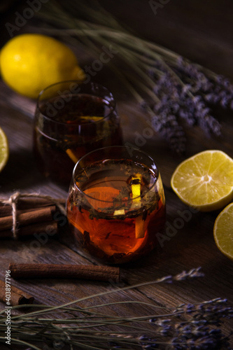 Transparent two cups with fragrant black tea, lemon, cinnamon and lavender on a natural background. Vintage wooden backdrop.