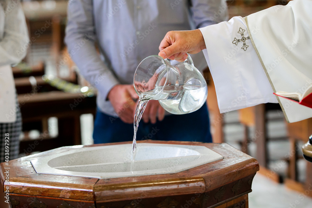 Priest pouring holy water into the baptismal font, moments before a