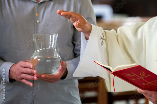 Obraz na płótnie Priest blessing holy water inside a jar that is held by a man's hands during a b