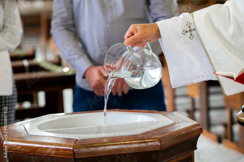 Stampa su tela Priest pouring holy water into the baptismal font, moments before a child receiv