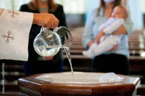 Fototapet Priest pouring holy water into the baptismal font, moments before a child receiv