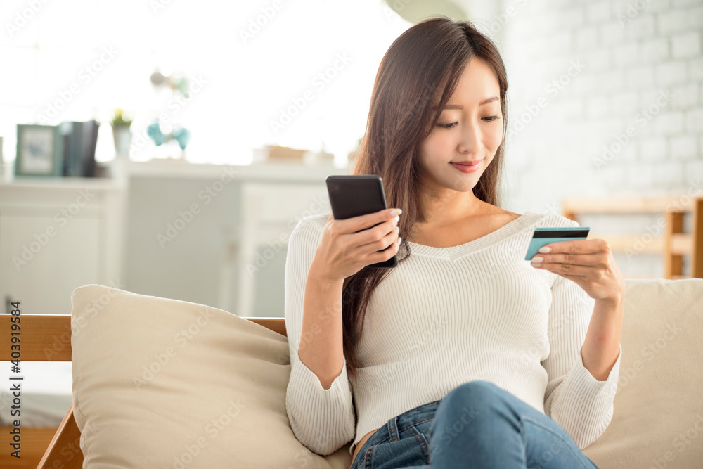 young woman buying online with  credit card and smart phone sitting on  couch at home