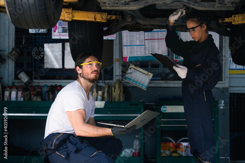 Engineer car mechanic under checking under the car by see detail in note book on hand for maintenance and fixed it.