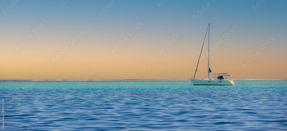 A sailboat on blue ocean water during a beautiful sunset