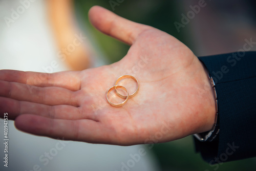 Two gold wedding rings lie on a man's open palm, close-up. Young groom holding wedding rings in his outstretched hand, blurred background.
