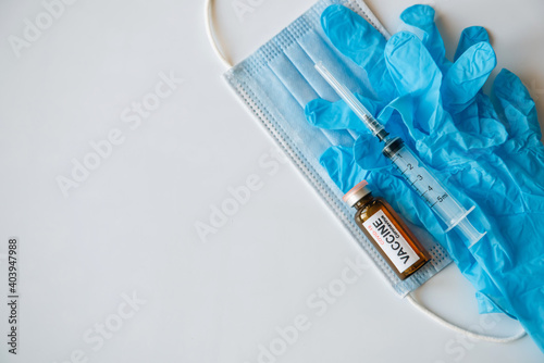Coronavirus COVID 19 vaccine vial and syringe on medical face mask and blue gloves, white background, copy space. World vaccination concept.