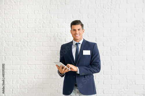 Elegant man in suit with blank badge and tablet computer near brick wall