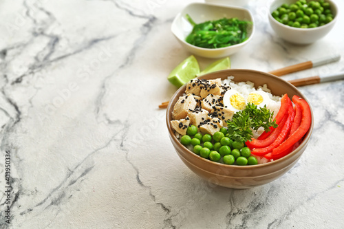 Bowl with tasty rice, chicken and vegetables on light background
