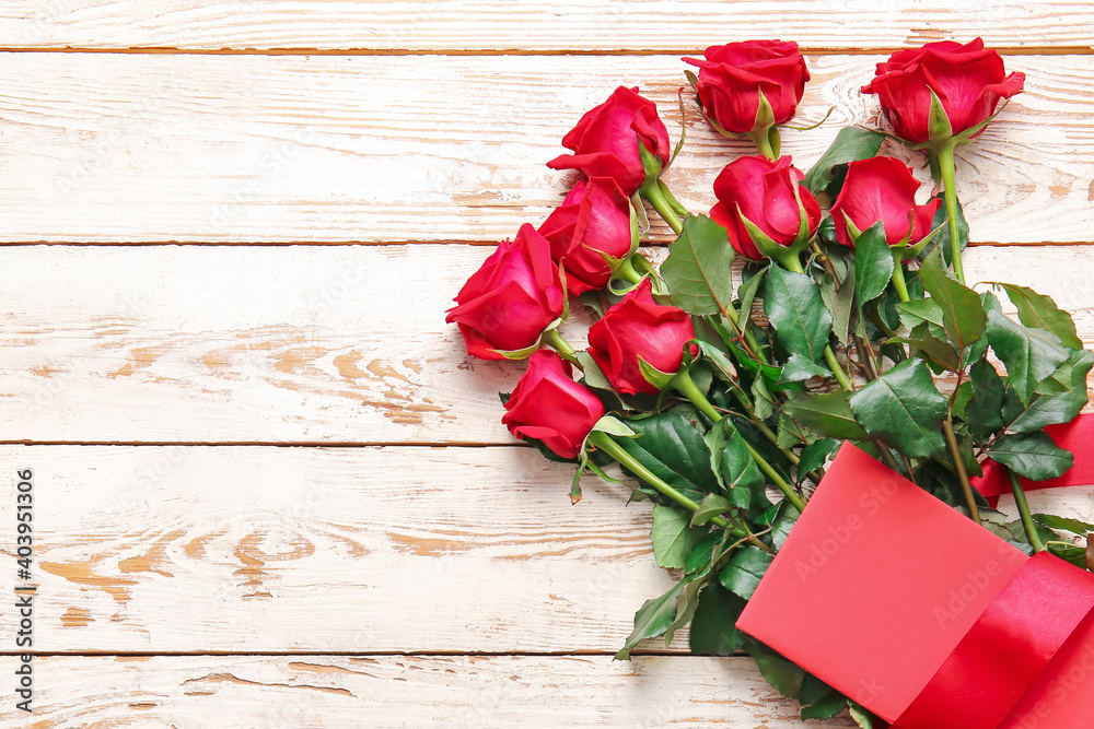 Bouquet of beautiful red roses and blank card on wooden background