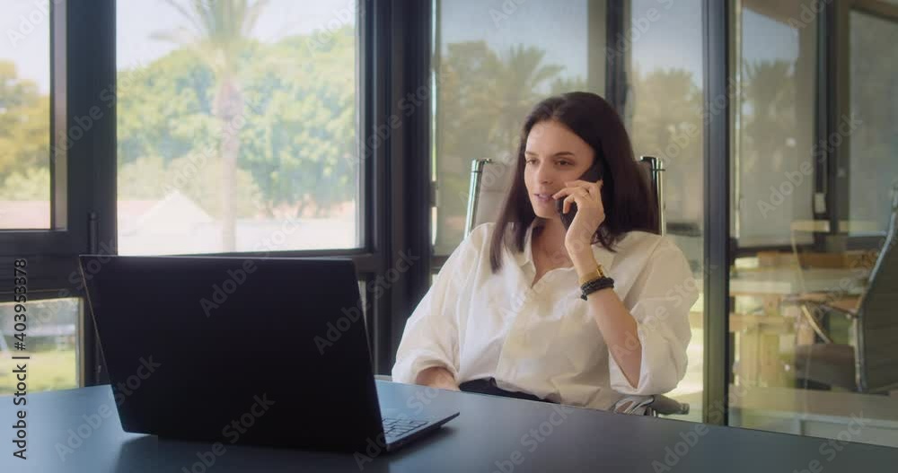 A businesswoman talking on the phone, smiling, while working at the office. A businesswoman talking on the phone, smiling, while working at the office.