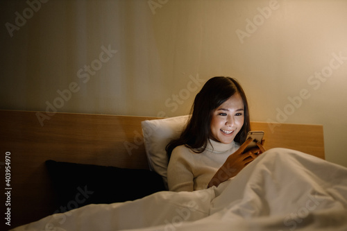 Smiling beautiful lady in white t-shirt on the bed using smartphone in the room © Rattanachoat