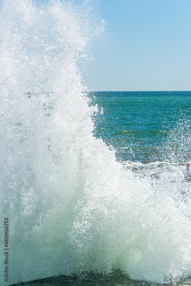 Fototapeta premium A huge sea wave breaks into splashes on the pier. Vertical photo