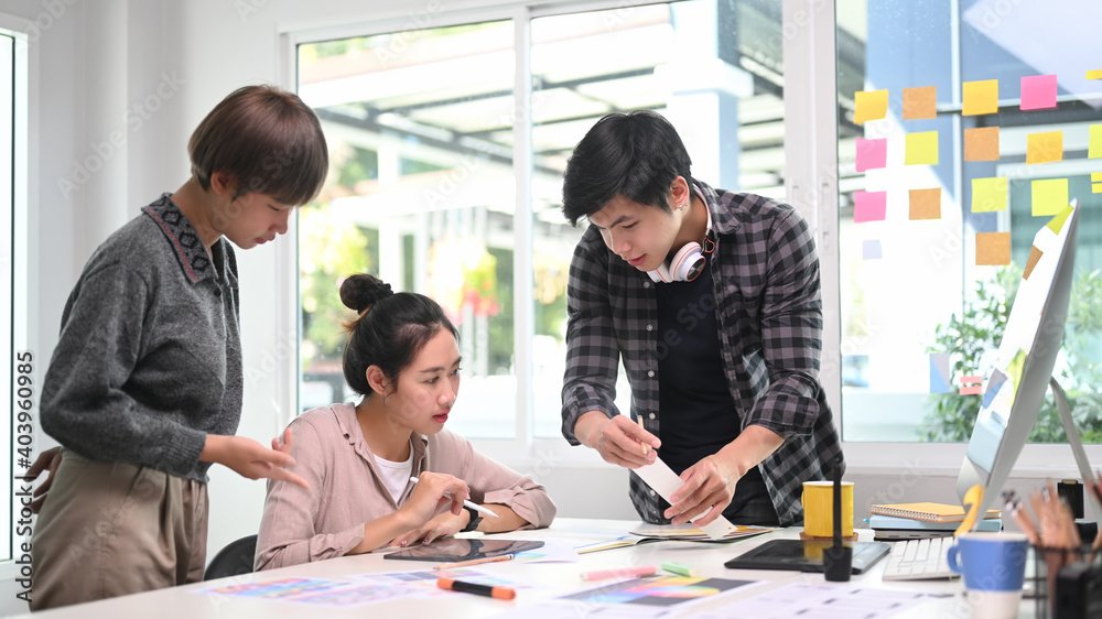 Group of designers in casual clothes working on project together and sharing ideas at creative office. Group of designers in casual clothes working on project together and sharing ideas at creative office.