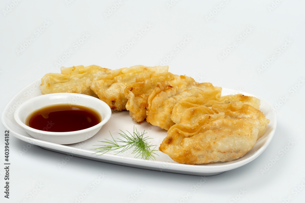 Tilted side view of Gyoza served on a long white plate and ready with soy sauce. Isolated white background.
