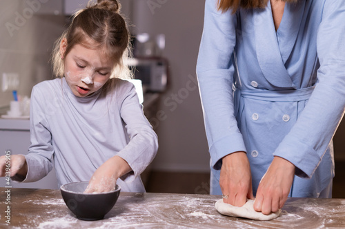mom and daughter together in the kitchen knead the dough while standing at the table. A woman is preparing a pizza or pastry.