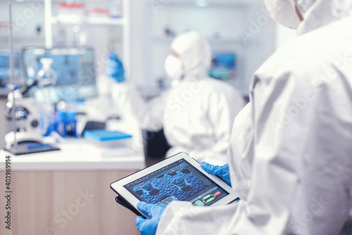 Medical engineer developing vaccine for coronavirus using tablet pc wearing ppe suit. Team of scientists conducting vaccine development using high tech technology for researching treatment against
