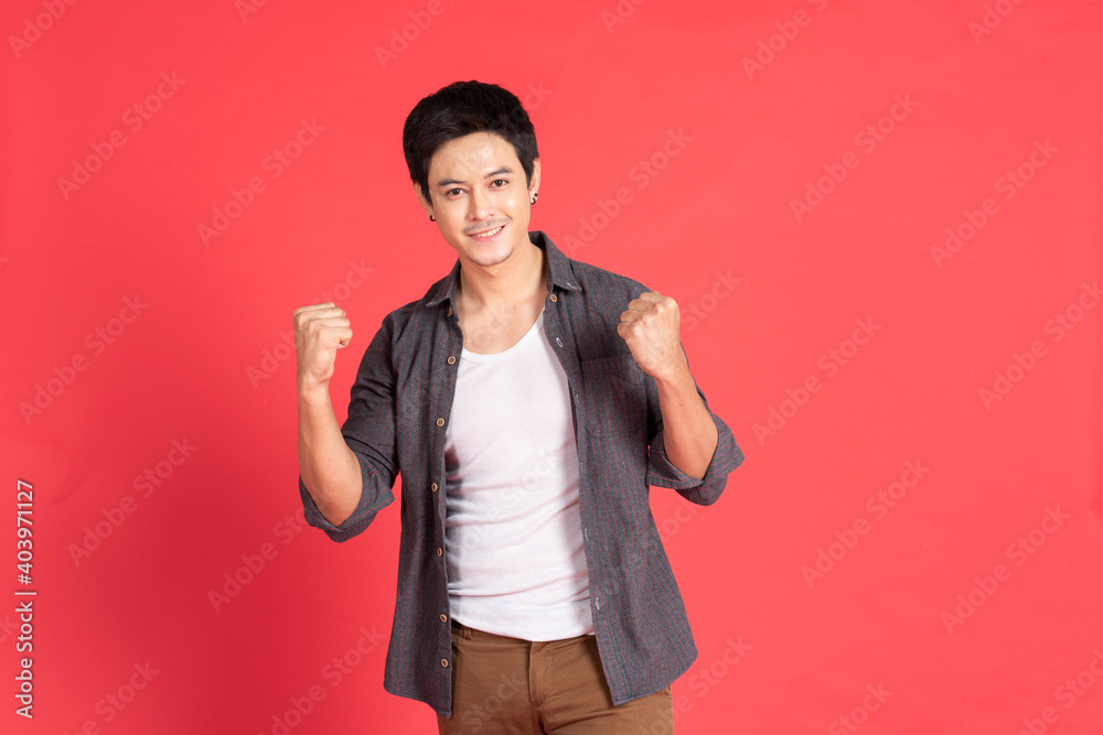 Happy young asian man in casual dress celebrates with two hand in the air on isolate red background. Happy young asian man in casual dress celebrates with two hand in the air on isolate red background.