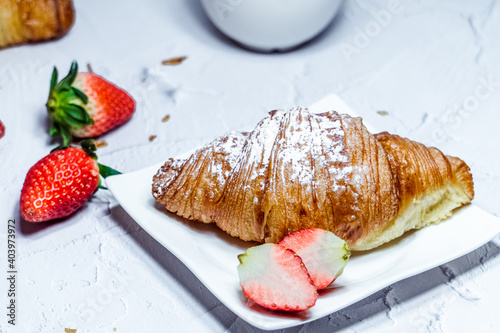A continental breakfast consisting of croissants sprinkled with icing sugar and fresh strawberries.