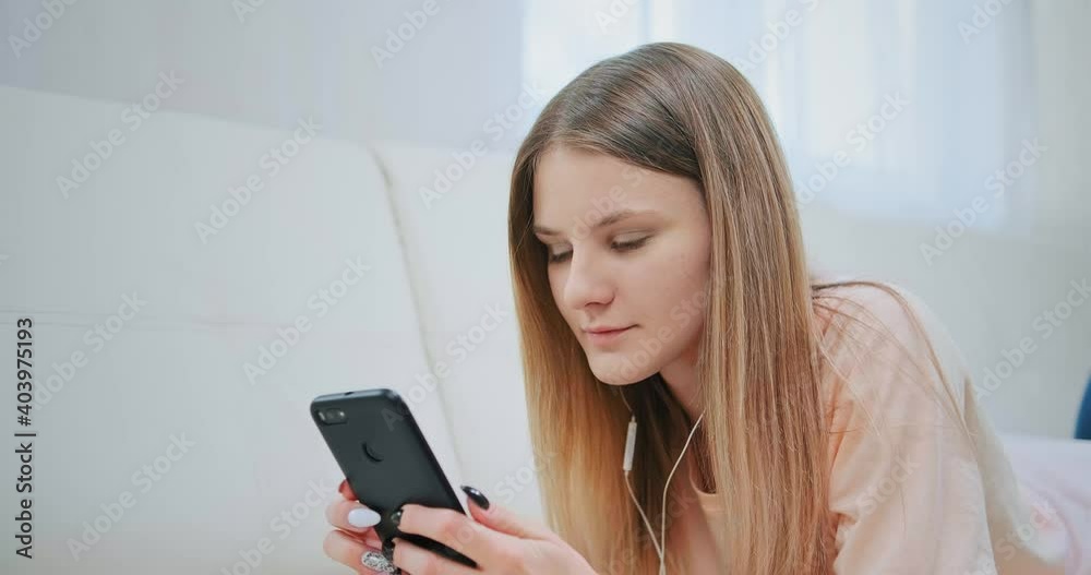 Concentrated lady with long loose fair hair orders in internet shop listening to music via smartphone staying home at isolation Concentrated lady with long loose fair hair orders in internet shop listening to music via smartphone staying home at isolation