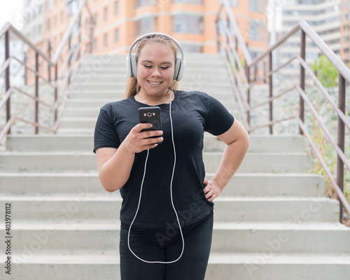 A fat young woman goes down the stairs and listens to music on a smartphone.