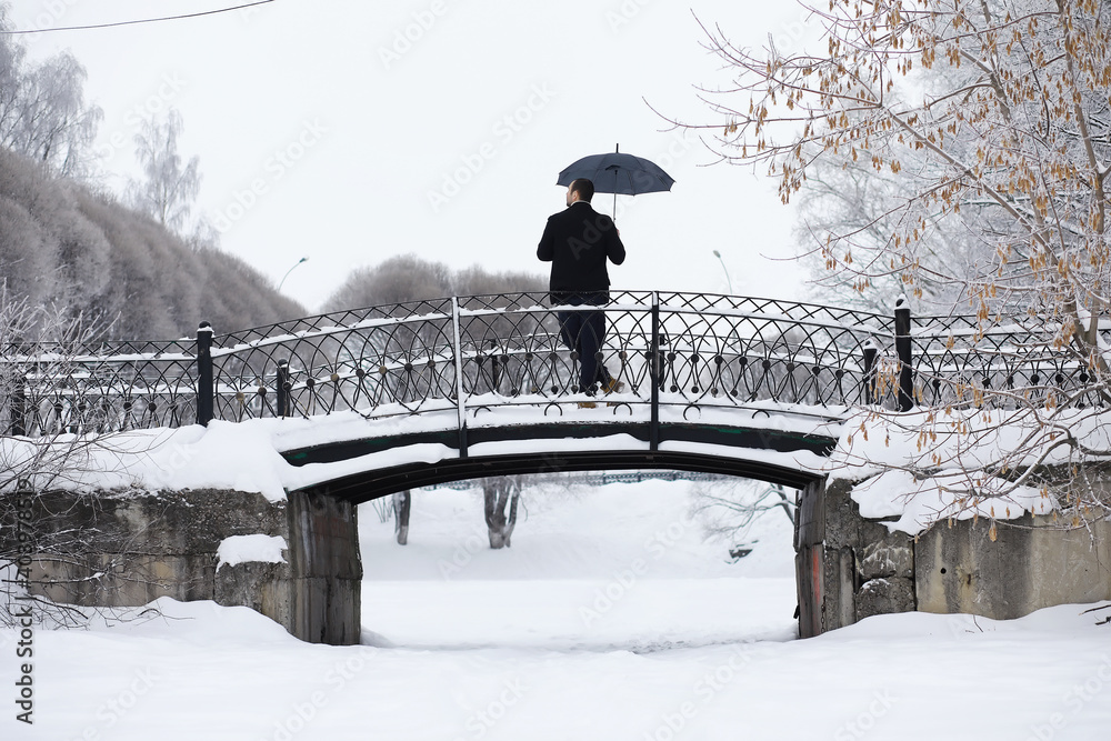 Fototapeta premium Winter walk with an umbrella.Man in a coat with an umbrella, walk against the backdrop of the winter landscape, winter view