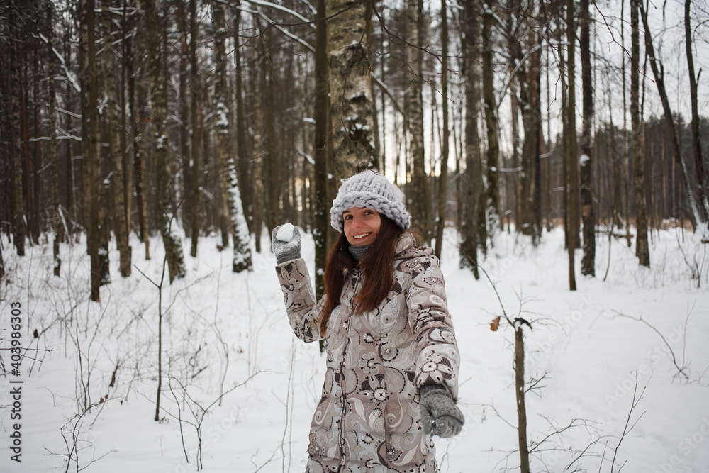 young woman plays snowballs in winter nature. Girl is dressed in a beige down-padded coat and knitted gray hat. young woman plays snowballs in winter nature. Girl is dressed in a beige down-padded coat and knitted gray hat.