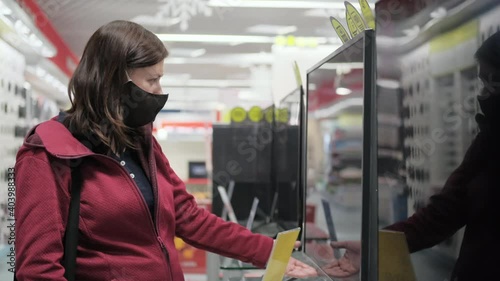 Woman in protective mask against virus buys new TV in store of gadgets and electronic devices. Woman jokes by imitating singing in karaoke photo