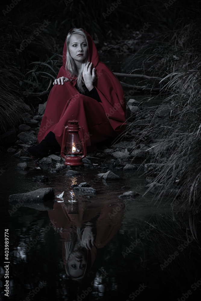Obraz premium Attractive woman dressed a little red riding-hood cross stream in a dark forest with a lantern