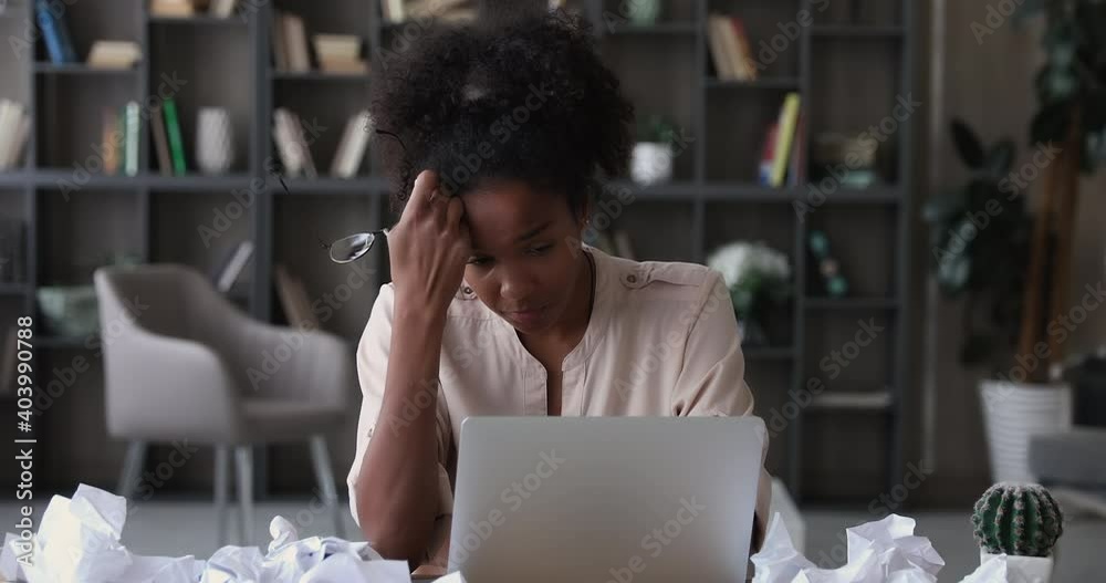 Stressed african business woman sit at desk with laptop and crumpled papers, feels tired take off glasses, having concentration problem, lack of ideas, writers block, creative crisis, deadline concept