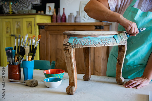 Carpenter craftswoman repainting old antique table in furniture workshop