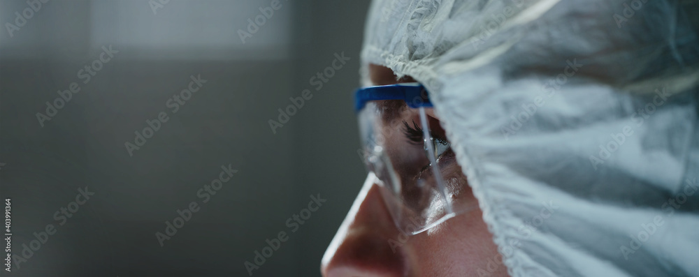 Close-up of female laboratory worker wearing safety goggles and overalls covering her head. Concept of viral vaccine developers working hard to create potential or efficient anti-coronavirus vaccine