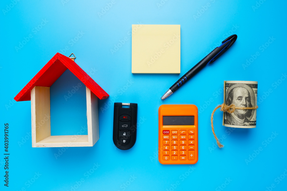 A picture house miniature, with fake money, copyspace notepad, car key, calculator, and pen on blue background. A picture house miniature, with fake money, copyspace notepad, car key, calculator, and pen on blue background.