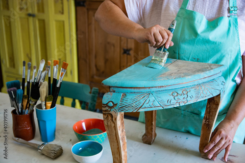Close-up of woman's hands painting old table in carpentry workshop