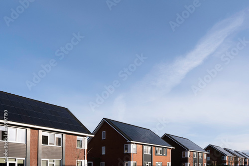 Solar panels mounted on the roofs of a row modern new-build houses in Lemmer, Friesland, the Netherlands with blue sky © Henk Vrieselaar